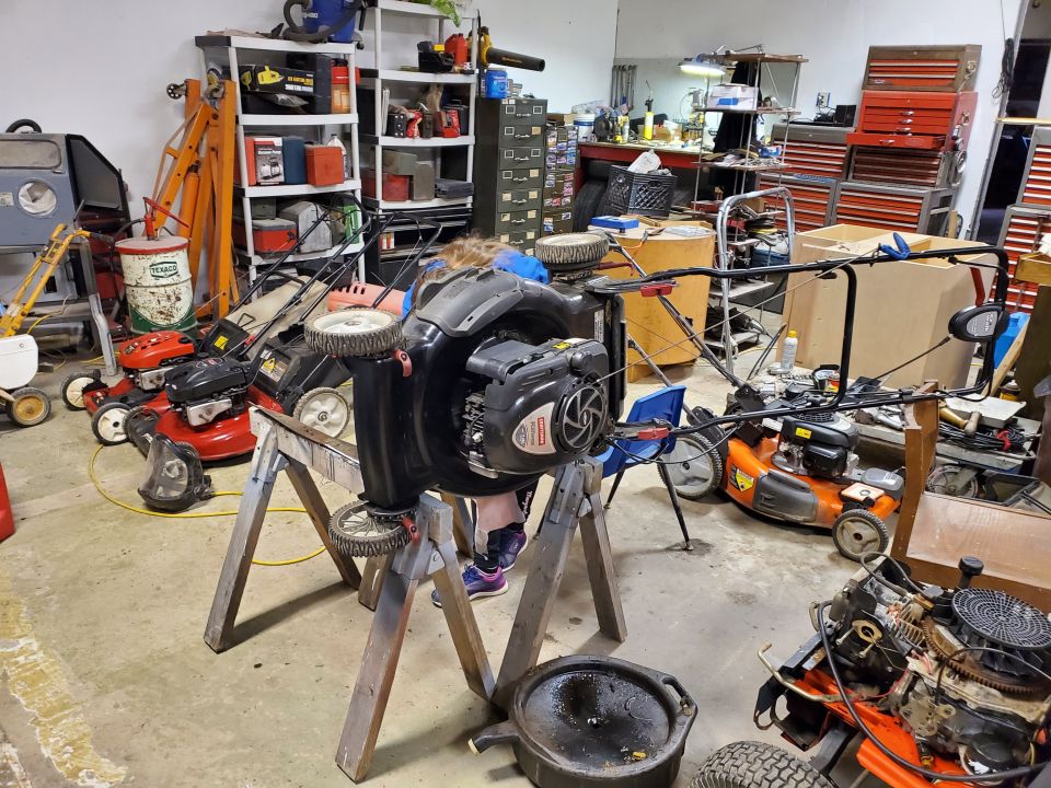 Lawn mower engine on a stand in a cluttered workshop garage