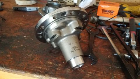 1985 Ford Bronco - A close-up view of a metal differential housing with markings '22 L 18 52825 913A588 HT Made in Taiwan' rests on a wooden workbench alongsi…