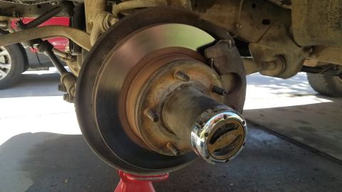 1985 Ford Bronco - A close-up view of a vehicle's front wheel hub assembly, showing a rusty brake rotor, caliper, and a chrome Warn locking hub. The vehicle i…
