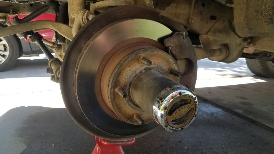 Close-up of a vehicle's front wheel hub with a rusty brake rotor and a chrome Warn locking hub.
