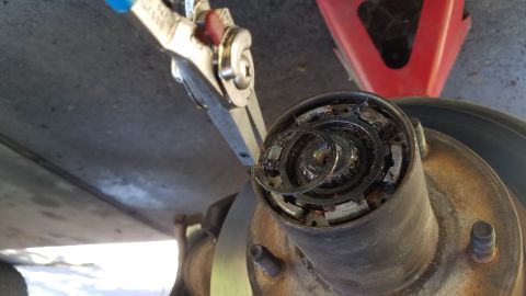 1985 Ford Bronco - A close-up view shows a mechanic using pliers to remove a damaged hub assembly from a vehicle. The hub assembly appears to be heavily greas…