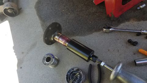 1985 Ford Bronco - A slide hammer is attached to a greased axle shaft with a flange. Tools and parts are laid out on a concrete surface.