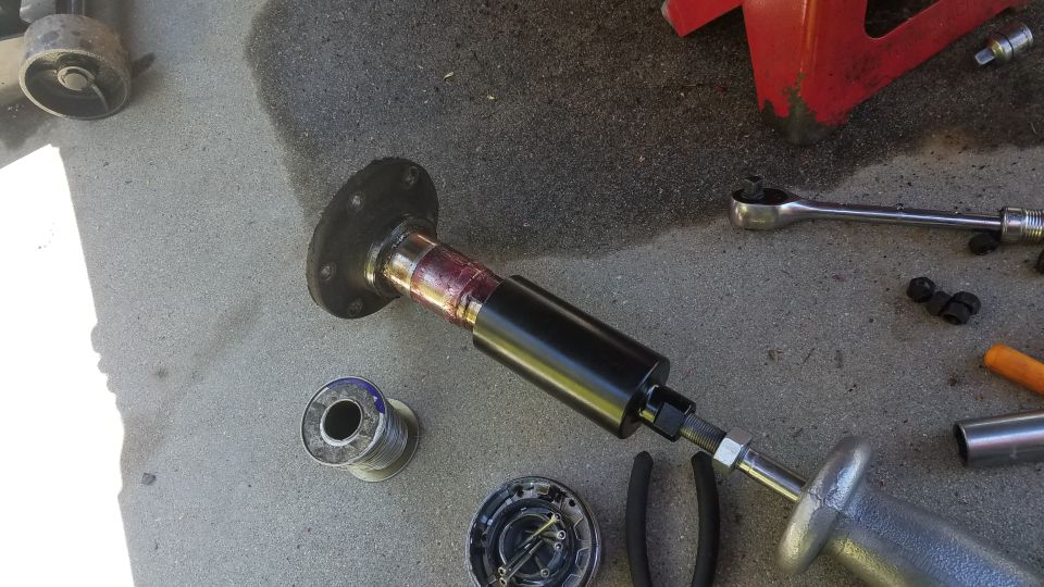 Slide hammer attached to greased axle shaft with flange, tools on concrete.