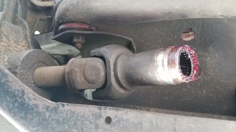 1985 Ford Bronco - A close-up view of a vehicle's driveshaft and universal joint, showing a splined shaft coated in red grease.