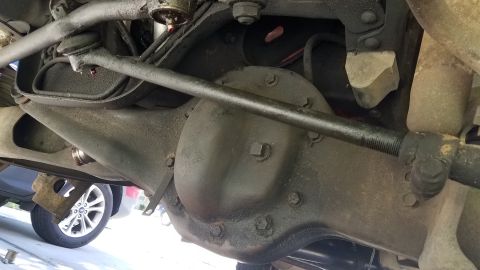 1985 Ford Bronco - Underside view of a vehicle's rear differential and suspension components, showing a dark-colored differential housing, steering linkage, a…