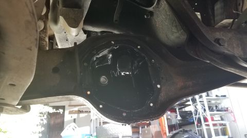 1985 Ford Bronco - The underside of a vehicle shows a differential housing with the cover removed, revealing the internal gears coated in dark fluid. The hous…