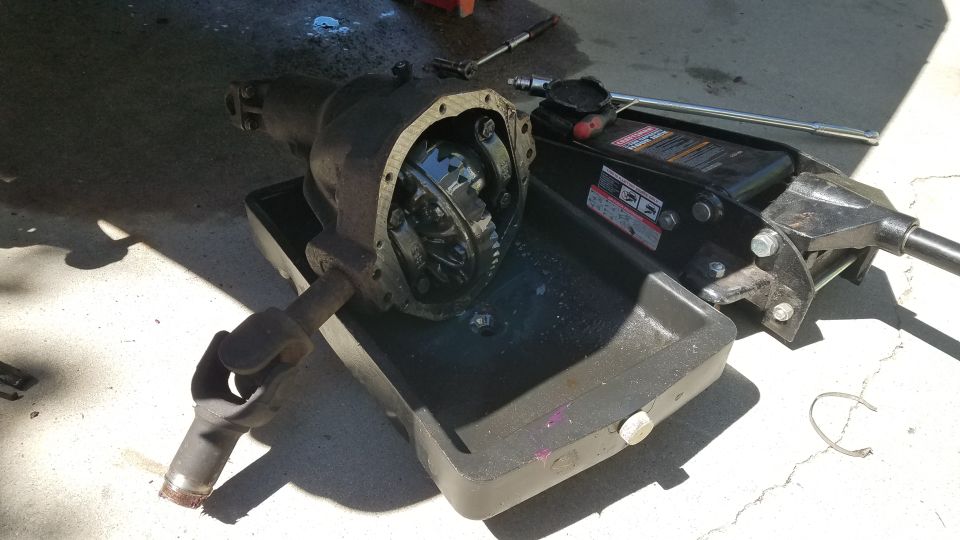 Differential housing with internal gears visible, in an oil drain pan with a jack and wrench.