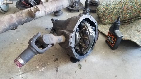 1985 Ford Bronco - A differential housing with a driveshaft attached is on the floor next to a bottle of hydraulic jack oil. The differential appears to be fr…