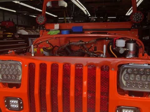 1992 Jeep Wrangler - Front view of an orange Jeep Wrangler with its hood open, revealing the engine bay and various wiring. The vehicle features aftermarket LED…