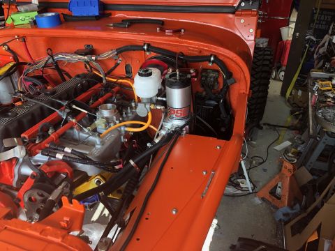 1992 Jeep Wrangler - Close-up view of the engine bay of an orange Jeep Wrangler, showing the engine, wiring, and various components. The vehicle is in a worksho…