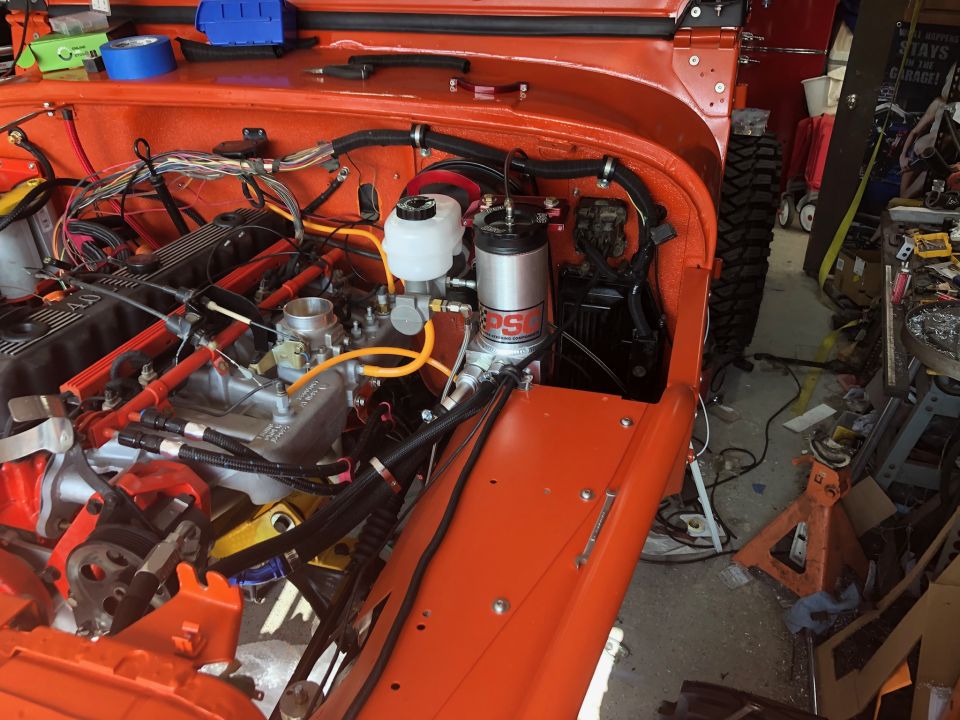 Orange Jeep Wrangler engine bay with engine, wiring, and components visible. Workshop setting.