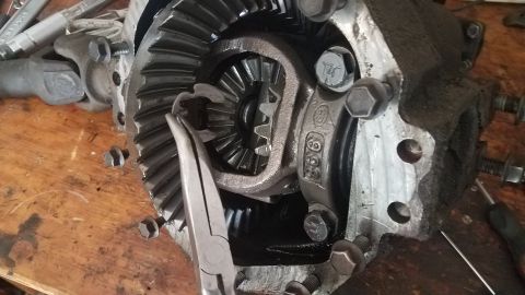 1985 Ford Bronco - A close-up view of a differential assembly with a pair of pliers holding a small gear. The assembly is resting on a wooden surface with var…