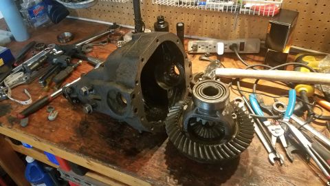 1985 Ford Bronco - A disassembled differential housing and ring gear are laid out on a wooden workbench alongside various tools, including pliers, wrenches, a…