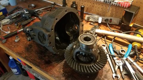 1985 Ford Bronco - A disassembled differential sits on a wooden workbench alongside various tools. The differential housing is open, revealing internal gears,…