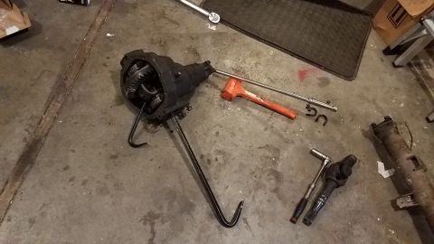 1985 Ford Bronco - A differential assembly with internal gears is shown on a concrete floor, along with various tools including a large orange mallet, a metal…