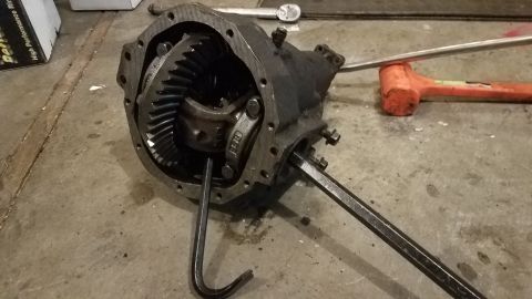 1985 Ford Bronco - A differential housing with gears is on a concrete floor, with a rubber mallet and a torque wrench visible in the background. Two metal too…