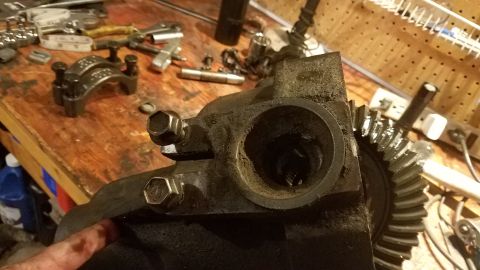 1985 Ford Bronco - A close-up view of a greasy differential housing with a large ring gear attached. Several tools and parts are scattered on a wooden workben…