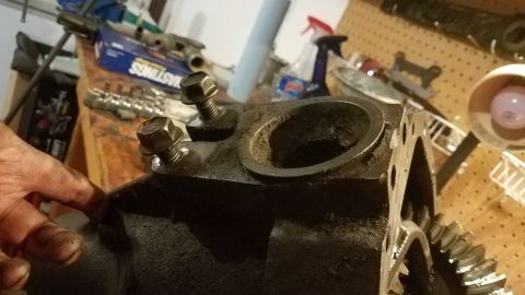 1985 Ford Bronco - A close-up view shows a greasy, cast-iron differential housing with two bolts securing a metal ring. Gears are visible inside the housing.