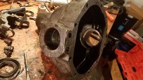 1985 Ford Bronco - A heavily used, cast iron differential housing sits on a wooden workbench surrounded by tools and disassembled parts. The housing is open,…