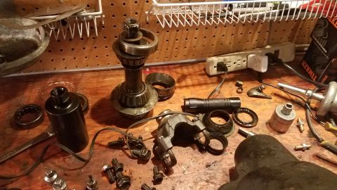 1985 Ford Bronco - A collection of automotive parts and tools are laid out on a wooden workbench. Visible items include bearings, a flashlight, bolts, a wrenc…