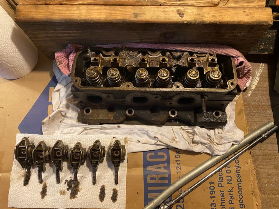 Disassembled engine cylinder head and rocker arms on a workbench.