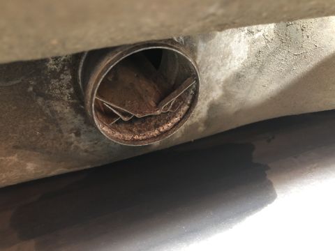 1980 Ford Bronco - A close-up view of a rusty, circular metal component, possibly part of an exhaust system, attached to the underside of a vehicle.