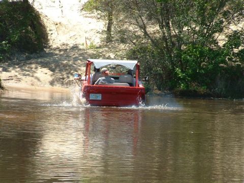 1986 Ford Bronco - A red off-road vehicle navigates through shallow water on a sunny day.