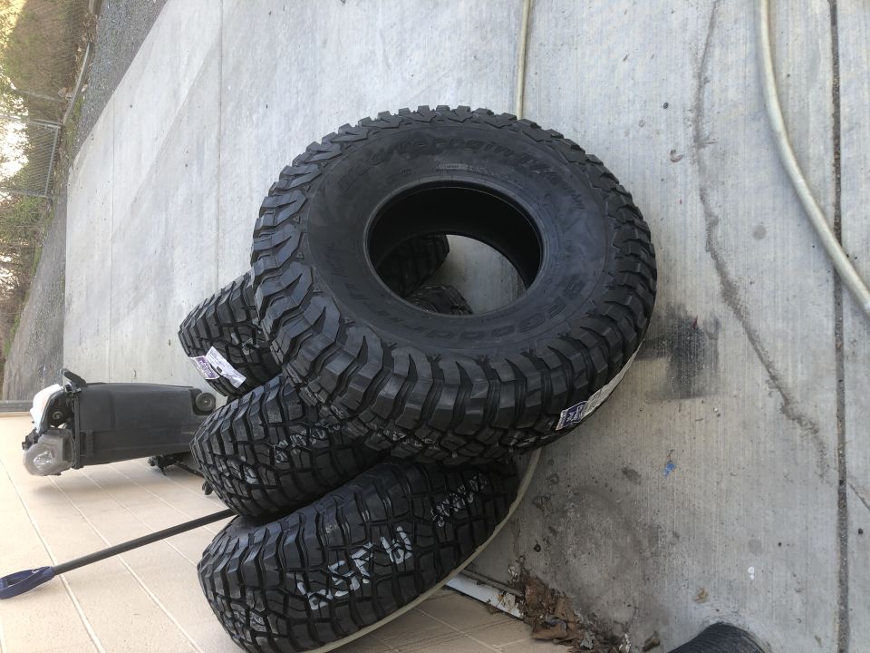 Stack of four BFGoodrich Mud-Terrain T/A KM3 tires leaning against a concrete wall.