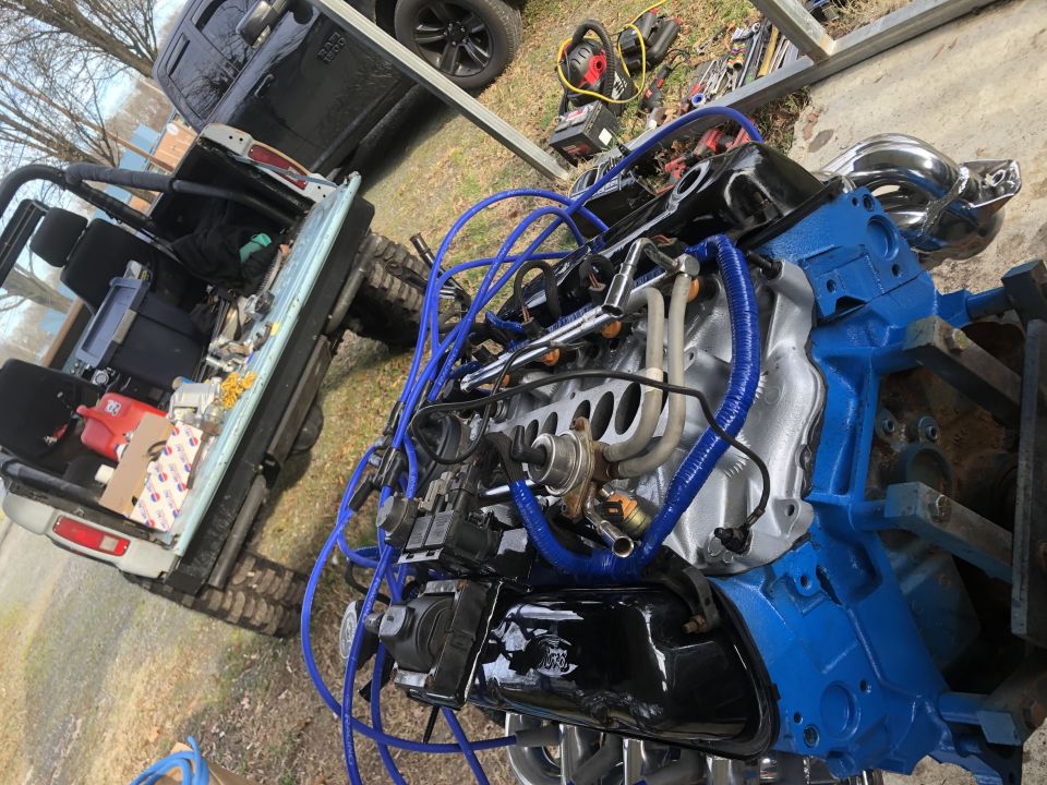Blue and silver V8 engine with blue spark plug wires next to a pickup truck bed.
