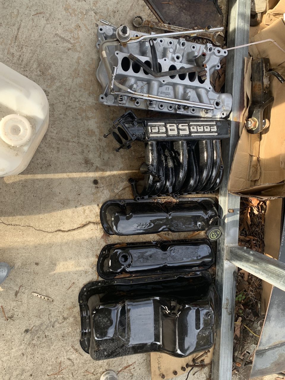 Engine parts including intake manifold, valve covers, and oil pan on concrete.