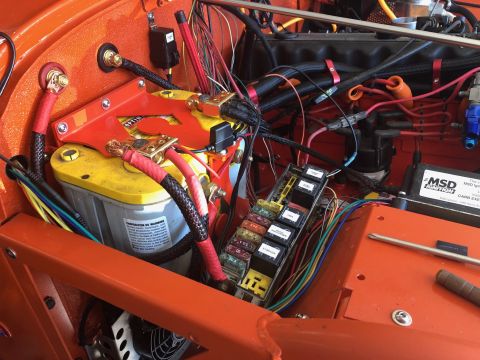 1992 Jeep Wrangler - The engine bay of an orange Jeep Wrangler shows a custom battery setup with an Optima battery, a fuse box, and various wiring harnesses con…