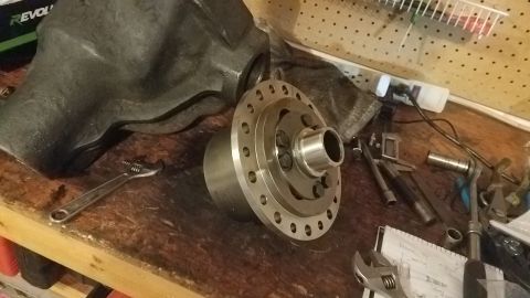 1985 Ford Bronco - A differential part with a bolt circle and a large, dark metal housing are on a wooden workbench. Tools including an adjustable wrench and…