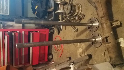1985 Ford Bronco - Two steel axle shafts with flanged ends are laid out on a concrete floor next to a red tool chest and a differential housing. Various weigh…