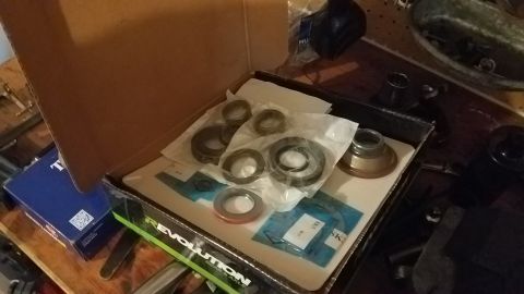 1985 Ford Bronco - A box of assorted automotive bearings and seals is laid out on a wooden surface. The box is open, revealing several parts packaged in plast…