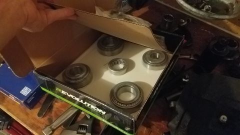 1985 Ford Bronco - A hand is opening a cardboard box that contains several metal bearings. The box has the text "REVOLUTION GEAR AXLE" visible on its side.