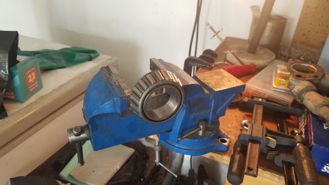 1985 Ford Bronco - A tapered roller bearing is held in a blue metal vise on a workbench. Various tools and parts are visible in the background.