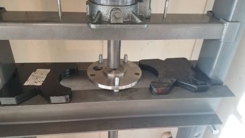 1985 Ford Bronco - A metal press is shown with a circular metal plate with four bolts attached to a central shaft. Two black, curved metal supports are positi…