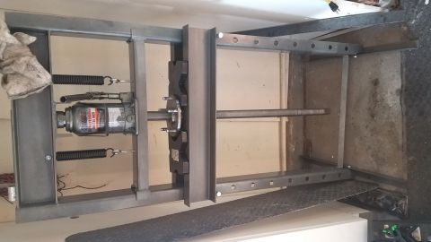 1985 Ford Bronco - A hydraulic bottle jack is positioned within a metal frame, likely a press, with a metal shaft extending through it. The frame appears to b…