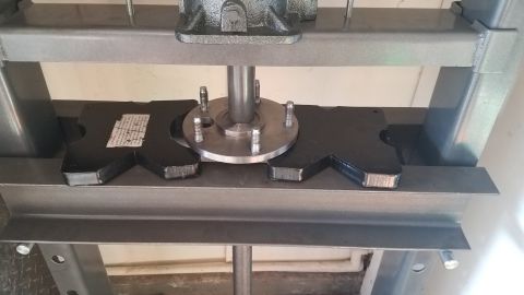 1985 Ford Bronco - A metal hub assembly with five bolts is being pressed into place by a hydraulic press. The assembly is supported by two black, custom-shape…