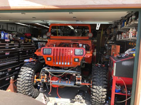 1992 Jeep Wrangler - An orange Jeep Wrangler is parked inside a garage with its hood open, undergoing modifications. The vehicle features large off-road tires a…