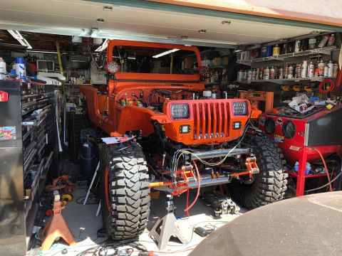 1992 Jeep Wrangler - An orange Jeep Wrangler is parked inside a garage, seemingly undergoing some modifications. The vehicle is elevated on jack stands, with it…