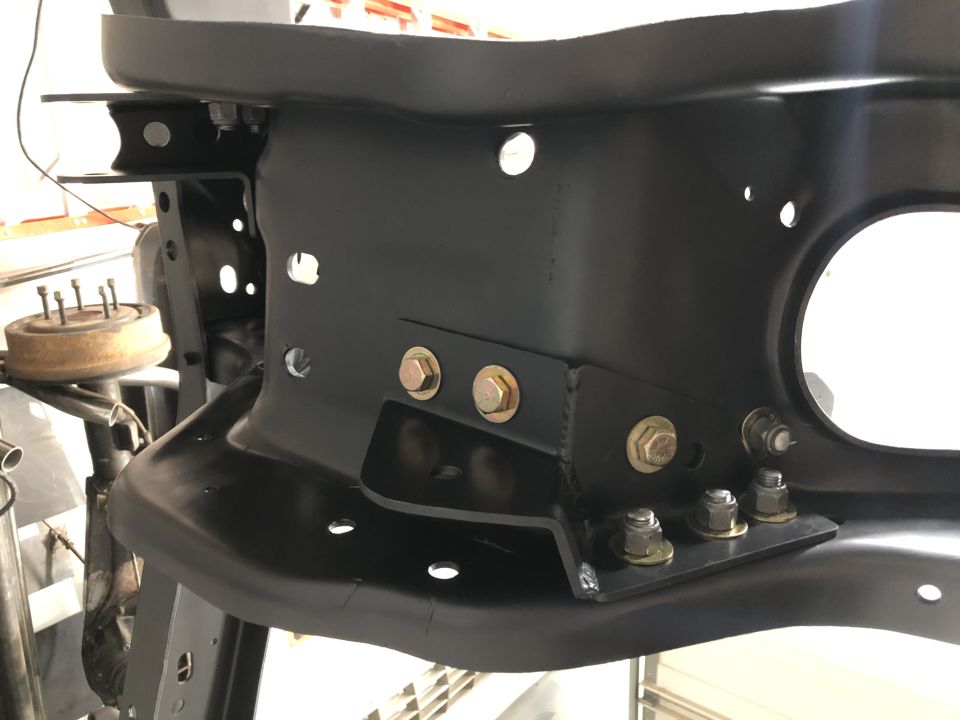 Black painted metal frame bracket with multiple bolts and holes, part of a vehicle's chassis