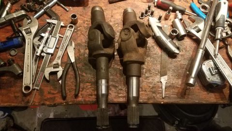 1985 Ford Bronco - A pair of driveshaft yokes sit on a wooden surface alongside an assortment of wrenches, pliers, and a caliper.