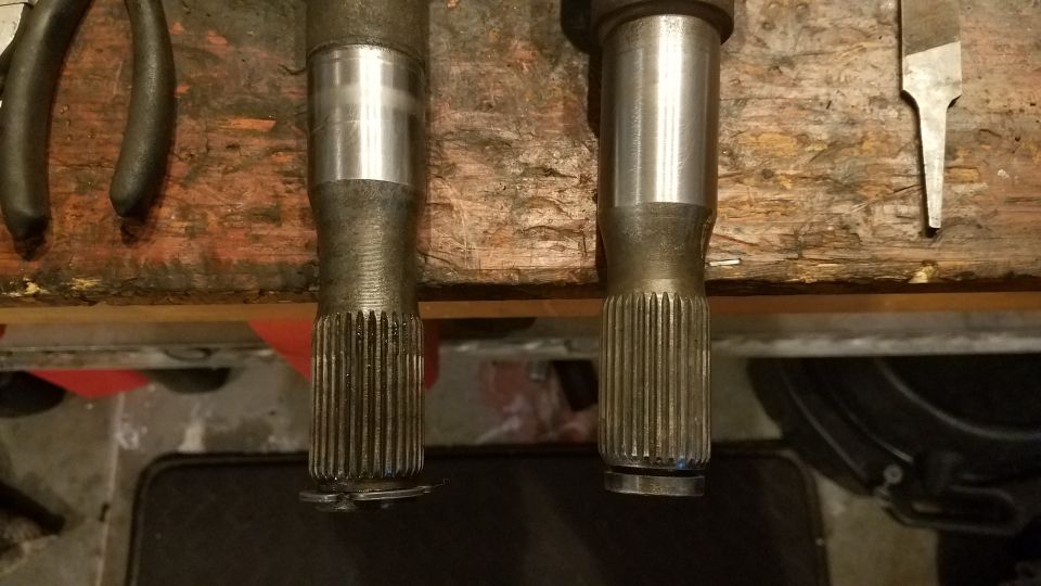 Two splined axle shafts resting on a wooden workbench with tools nearby