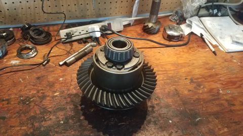 1985 Ford Bronco - Differential gear assembly with a bearing on top, resting on a wooden surface with tools and electrical components in the background.