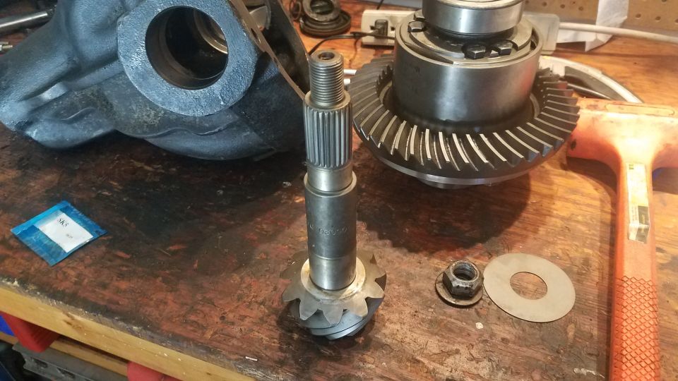 Differential gears, pinion shaft, and housing parts laid out on a workbench. Includes a nut and washer