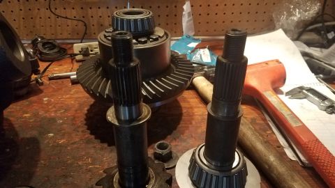1985 Ford Bronco - Differential gears and axles are laid out on a workbench, alongside tools like hammers and a caliper.