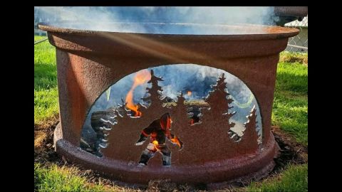 1985 Toyota Hilux - A rustic fire pit features a cutout silhouette of Bigfoot amidst a forest scene, with flames burning within.