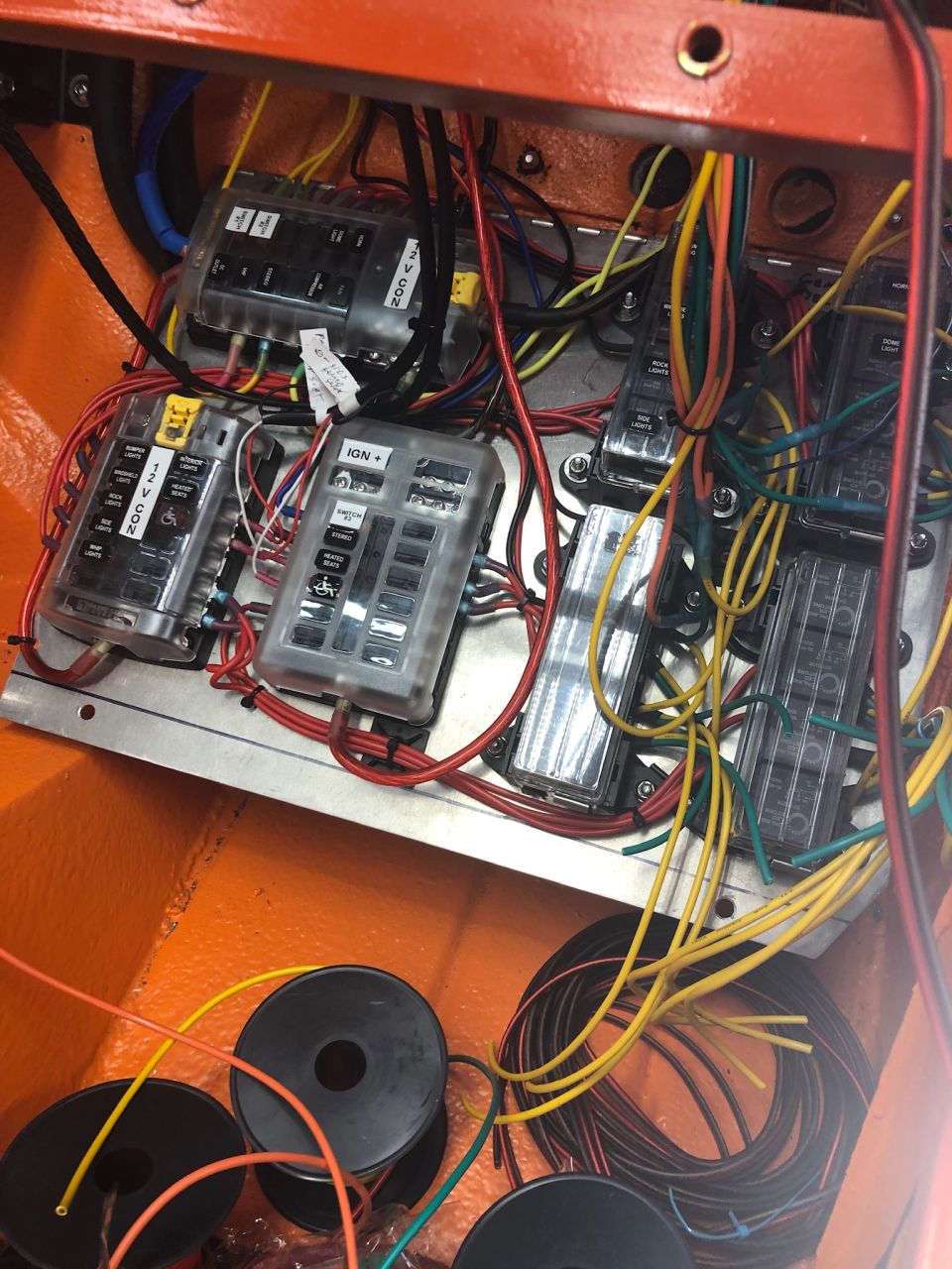 Close-up of a vehicle's electrical fuse box with multiple clear-covered fuse blocks and a tangle of red, yellow, and green wires