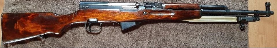 Wooden stock rifle with metal components, laid horizontally on a textured surface